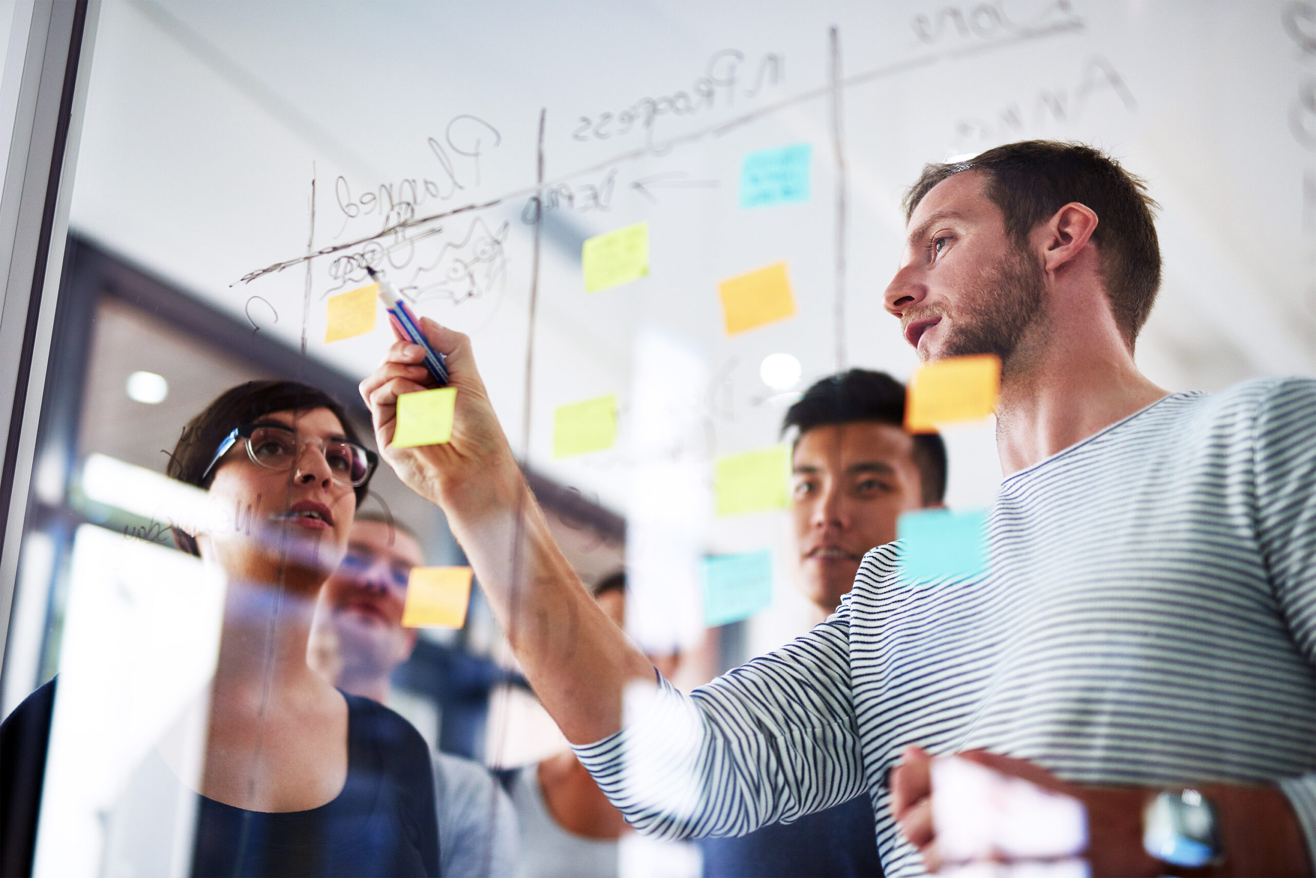 Cropped shot of coworkers using sticky notes on a glass wall during a meeting