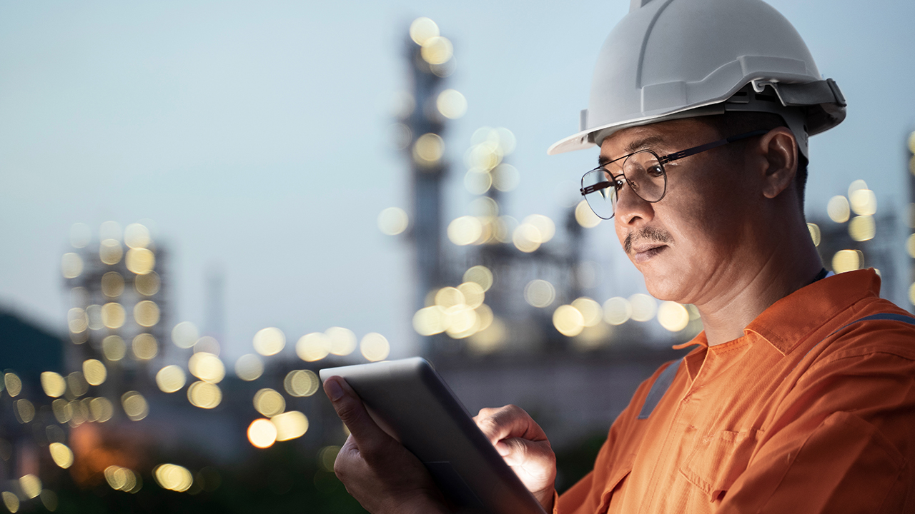 man wearing a helmet using a tablet computer infront of a chemical site