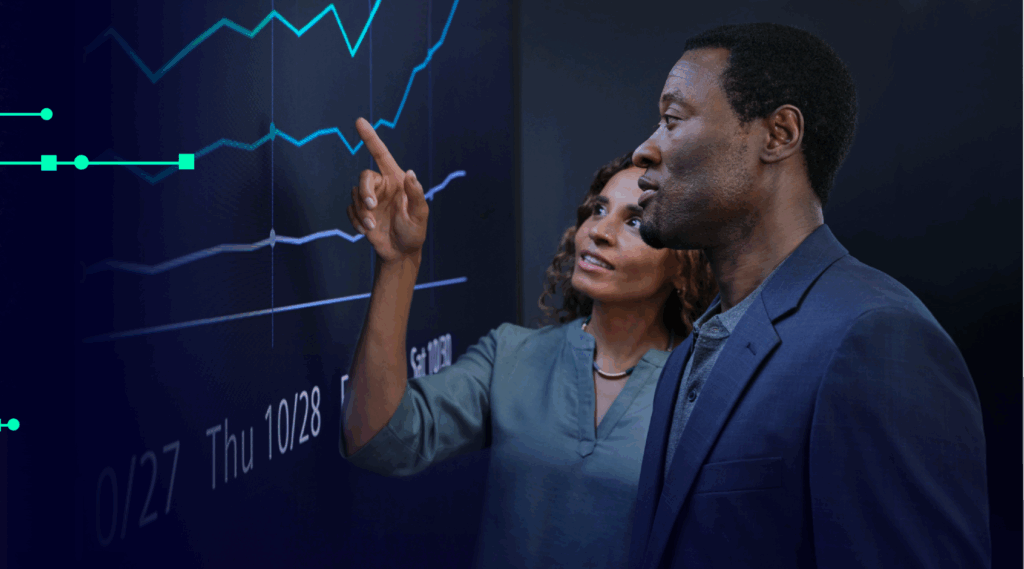 A woman and a man review data visualizations on a large digital screen, discussing product optimization and insights that support the product optimization process.