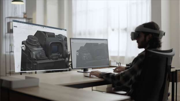 Designer examining a high‑fidelity 3D CAD camera model on two screens and in VR within a Sony immersive engineering setup.