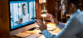 Caucasian business man talking with african male partner coach on video conference call discussing social distance work at virtual remote meeting videoconference chat using pc computer at home office.