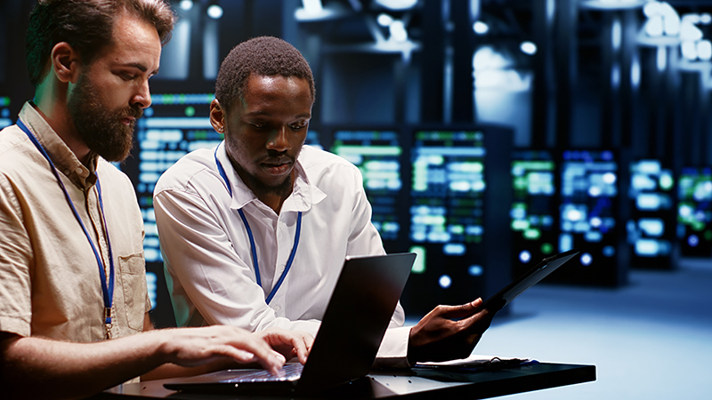 Two HPCWorks administrators looking at a laptop and a tablet with a computer data center in the background